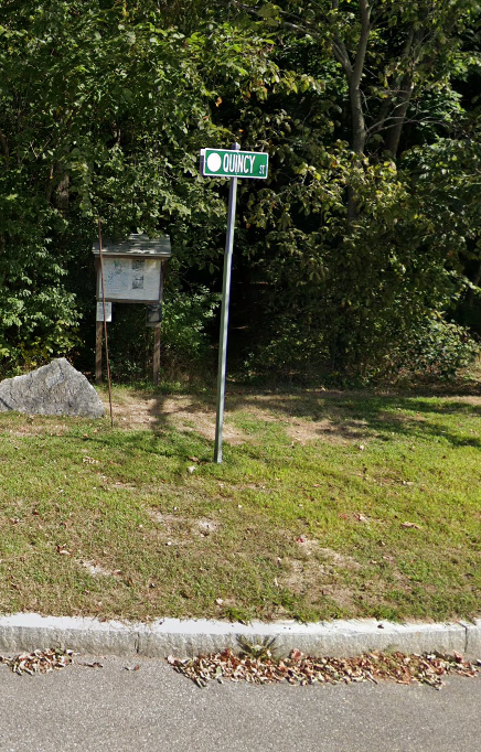 The entrance to massapoag trail with a kiosk next to a street sign that says "Quincy Street".